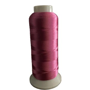 Op de afbeelding: Een spoel levendig magenta garen. De draad is strak gewikkeld rond een cilindrische kern, met een gladde, glanzende textuur. De spoel heeft een witte basis en een witte bovenkant, wat een helder contrast biedt met de kleur van de draad. Ideaal voor naai- en knutselprojecten.