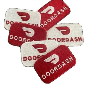 May include: A collection of rectangular embroidered patches featuring the DoorDash logo and text. The patches alternate between red backgrounds with white stitching and white backgrounds with red stitching, all with rounded corners and a textured finish.