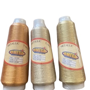 May include: Three spools of metallic thread in gold, silver, and copper colors. Each spool is labeled "OMEGA Embroidery Supplies" and has the text "Metallic Yarn" printed on the label. The spools are 145 grams each.