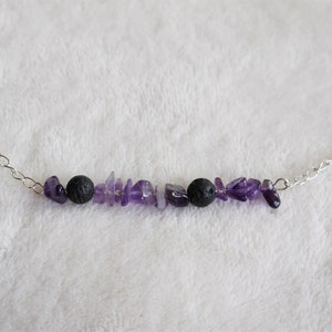 May include: A silver chain necklace with a purple amethyst and black lava rock bead charm.