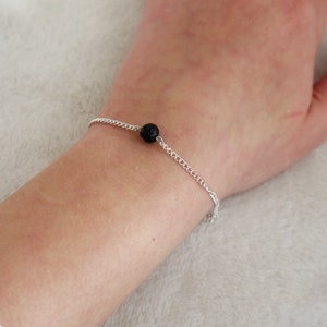 Può includere: Un braccialetto a catena d'argento con un solo ciondolo di pietra lavica nera.