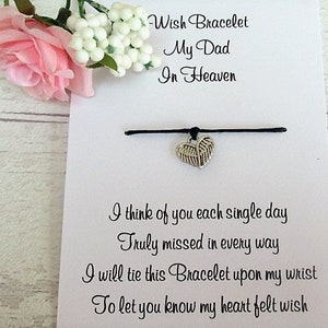 May include: A white card with black text that reads "Wish Bracelet My Dad In Heaven" and a poem about remembering a loved one. A black string bracelet with a silver heart charm is attached to the card.