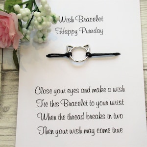 May include: A black string bracelet with a silver cat charm. The card reads "Wish Bracelet Happy Purrday" and includes instructions for making a wish. Close your eyes and make a wish. Tie this Bracelet to your wrist. When the thread breaks in two, then your wish may come true.