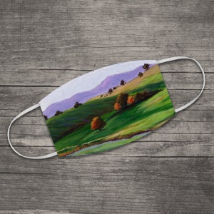 Puede incluir: Una mascarilla facial con una pintura de un paisaje verde y morado con árboles. El paisaje está pintado de forma estilizada con pinceladas.