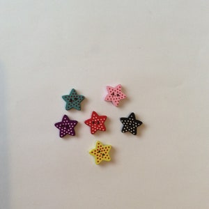 Puede incluir: Seis botones de madera en forma de estrella con lunares de varios colores, incluyendo rojo, rosa, amarillo, negro, morado y verde azulado.