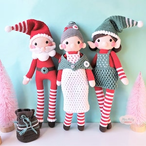 Op de afbeelding: Drie gehaakte elfpoppen, één gekleed als Sinterklaas, één in een witte jurk met een groene vest en één in een groene jurk met een rode vest. Alle drie de poppen hebben rood-wit gestreepte kousen en staan op een lichtblauwe achtergrond.