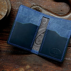 Op de afbeelding: Een blauwe leren portemonnee met een paisley-patroon aan de binnenkant. De portemonnee heeft meerdere kaartsleuven en een blauw stikdetail.