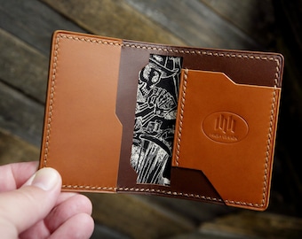 May include: A brown leather wallet with a stitched edge and a small pocket on the front. The wallet is open to reveal a brown leather interior with a card slot and a pocket for cash. The wallet has a logo that says "HIGH GRAIN" on the front.