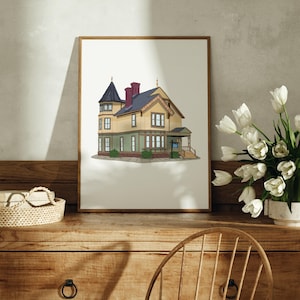 May include: A framed illustration of a yellow house with green trim and a blue door. The house has a steep roof with a grey roof and a red chimney. The house has a porch with a white railing and a blue sign that says "For Sale".