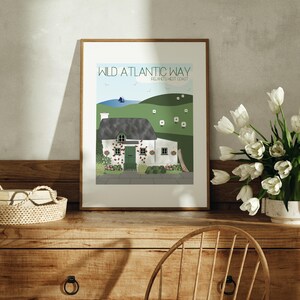 May include: A framed print of a white cottage with a green door and a thatched roof. The print is titled "Wild Atlantic Way, Ireland's West Coast".