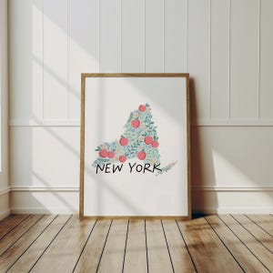 May include: A framed print of the state of New York, outlined in green leaves and pink apples. The text "NEW YORK" is printed below the outline.