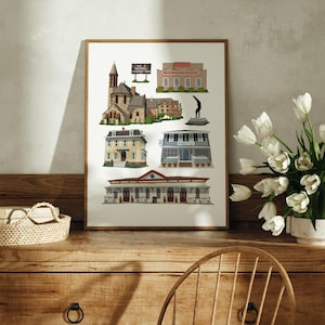 May include: A framed print with illustrations of buildings, including a church and a sign that reads "THIS IS MEDFORD A FRIENDLY TOWN". The artwork is displayed on a wooden surface. The print features a variety of architectural styles and colours.
