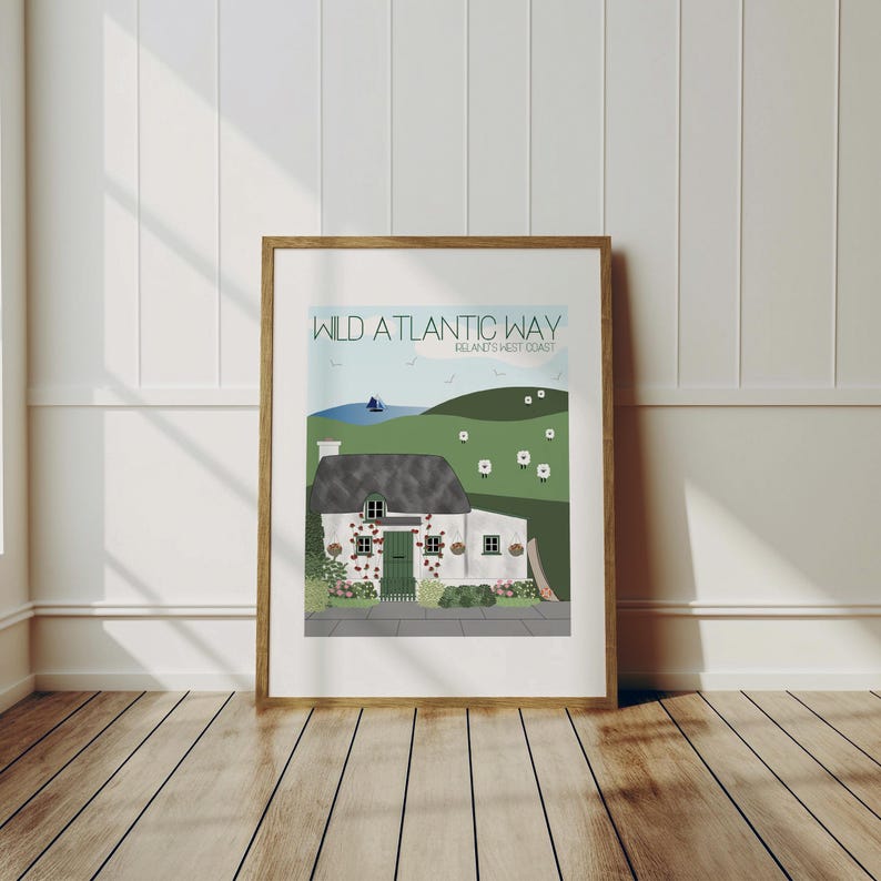 May include: A framed print featuring a white cottage with a green door and roof. The print includes the text "Wild Atlantic Way, Ireland's West Coast" at the top. The background is a green hill with white sheep.