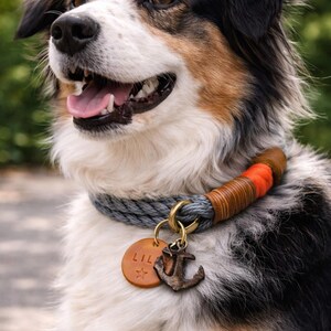 Op de afbeelding: Een driekleurige Australian Shepherd hond draagt een grijze touwhalsband met oranje en bruine lederen accenten. De halsband heeft een messing ring met een ronde, lichtbruine leren hanger gegraveerd met de naam LILA en een ster, plus een ankerbedel.