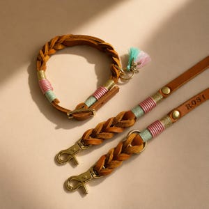 Könnte beinhalten: Ein Haustierhalsband und Leinen-Set aus hellbraunem Leder mit geflochtenen Lederabschnitten, goldfarbenen Metallbeschlägen und dekorativen Garnwicklungen in Pink, Minzgrün und Gold. Die Leine enthält ein Metallschild mit der Gravur ROSI.