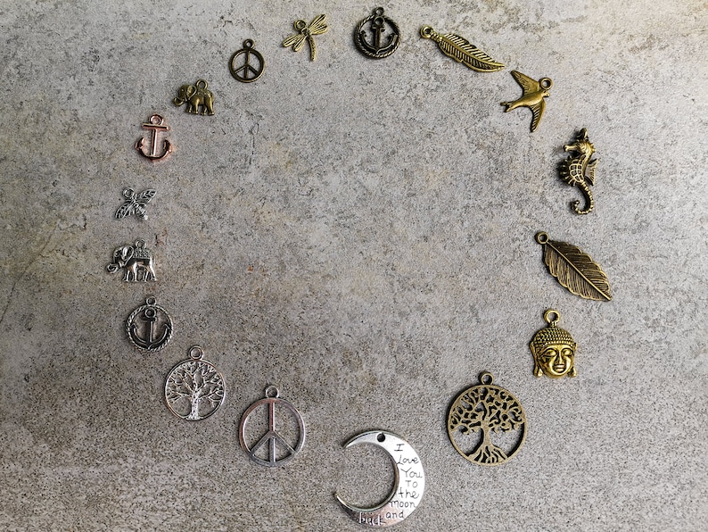 May include: A collection of metal charms arranged in a circle, including shapes of anchors, elephants, peace signs, dragonflies, feathers, birds, seahorses, trees, Buddha heads, and a crescent moon charm with the text I Love You to the moon and back.