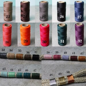 May include: A collection of spools of thread and cord segments labelled with numbers 23 through 50. The spools display various solid colours including brown, grey, black, blue, orange, red, green, and purple. The cord segments feature wrapped thread accents.
