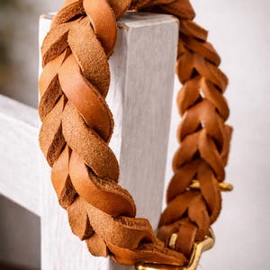 Peut inclure: Un collier en cuir beige dot&eacute; d'un design tress&eacute; &eacute;pais &agrave; la texture lisse. Le collier est fix&eacute; par une boucle en m&eacute;tal dor&eacute; poli, mettant en valeur une construction robuste et une couleur marron chaud uniforme sur toute la longueur.