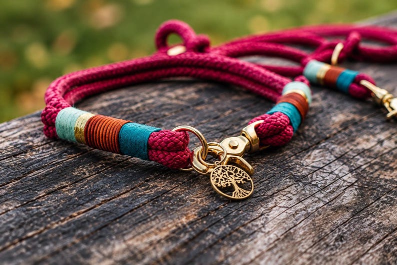 May include: A magenta rope dog collar featuring gold-toned metal hardware, a circular tree of life charm, and decorative thread wrappings in teal, orange, and light blue. The collar includes a sturdy metal clasp and a matching rope leash attachment.
