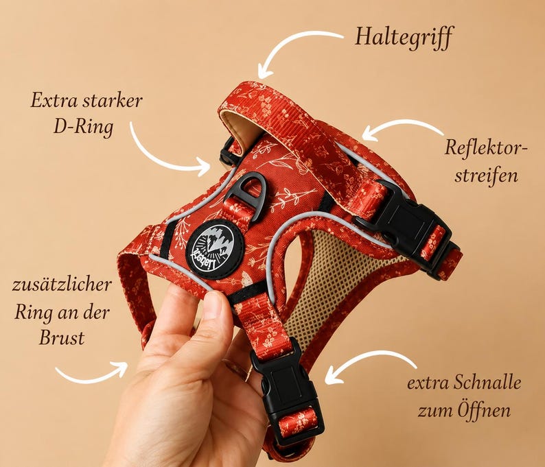 May include: A red pet harness featuring a white floral pattern, a top handle, reflective strips, black plastic buckles, and two D-rings. The harness includes a circular black logo patch with white mountain graphics and the text Liabert.