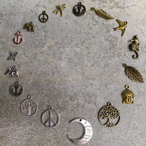 Pode incluir: Uma cole&ccedil;&atilde;o de berloques de metal dispostos em c&iacute;rculo, incluindo formas de &acirc;ncoras, elefantes, s&iacute;mbolos da paz, lib&eacute;lulas, penas, p&aacute;ssaros, cavalos-marinhos, &aacute;rvores, cabe&ccedil;as de Buda e um berloque de meia-lua com o texto I Love You to the moon and back.