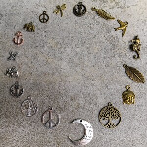 Peut inclure: Une collection de breloques en m&eacute;tal dispos&eacute;es en cercle, comprenant des formes d'ancres, d'&eacute;l&eacute;phants, de signes de paix, de libellules, de plumes, d'oiseaux, d'hippocampes, d'arbres, de t&ecirc;tes de Bouddha et un croissant de lune avec le texte I Love You to the moon and back.