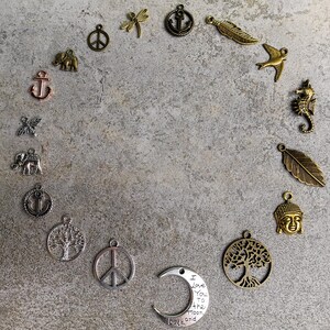 May include: A collection of assorted metal charms arranged in a circle, including shapes of anchors, elephants, peace signs, a dragonfly, feathers, a seahorse, a Buddha head, trees of life, and a crescent moon inscribed with I Love You To The Moon And Back.
