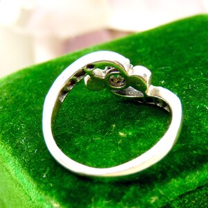 May include: A silver ring with a single clear stone set in a decorative design. The ring is displayed on a green velvet box.
