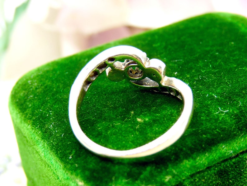 May include: A silver ring with a single clear stone set in a decorative design. The ring is displayed on a green velvet box.