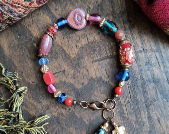 Pulsera de cuentas en tonos rojos, rosas y azules, con detalles dorados y cobre antiguo.