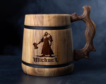 May include: Wooden beer mug with a dark handle and a detailed illustration of a warrior holding a hammer. The mug has a black band around the top and bottom. The name "Michael" is engraved below the warrior.