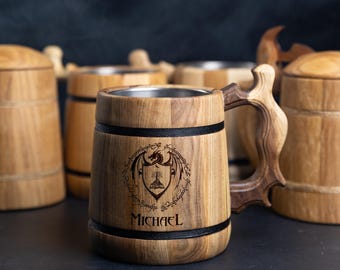 Può includere: Un boccale di birra in legno con una fascia nera e un design inciso a laser di un drago, un albero e il testo "Un anello per domarli tutti". Il boccale ha anche il nome "MICHAEL" inciso.