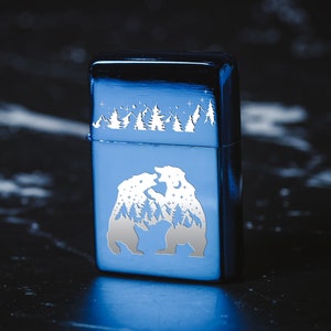 Puede incluir: Un encendedor de metal azul con un dise&ntilde;o grabado en blanco de dos osos enfrentados en un entorno de bosque. Los osos est&aacute;n rodeados de un cielo estrellado.