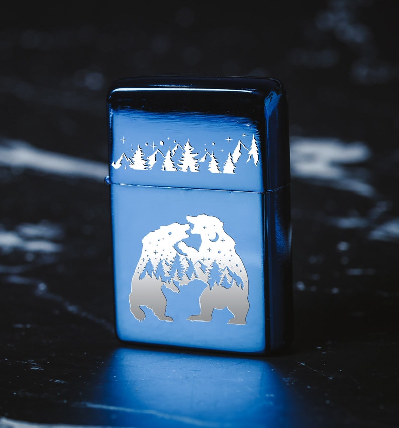 Puede incluir: Un encendedor de metal azul con un dise&ntilde;o grabado en blanco de dos osos enfrentados en un entorno de bosque. Los osos est&aacute;n rodeados de un cielo estrellado.