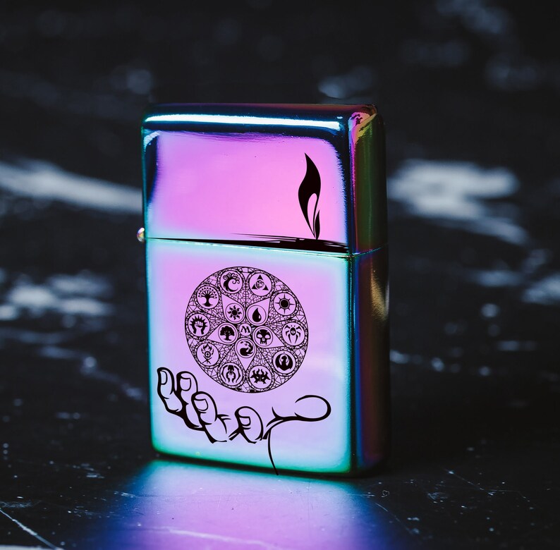 May include: A iridescent metal lighter with a black and white design of a circle with symbols inside. The lighter has a black flame design on the top.