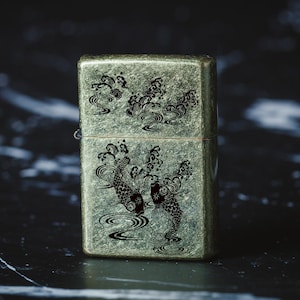 May include: A vintage-style lighter with a green metallic finish and an engraved design of two black koi fish swimming in a wave pattern.