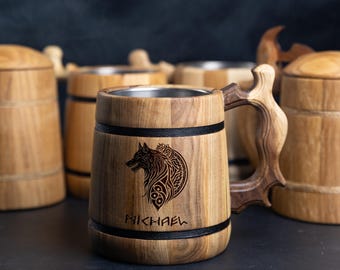 Può includere: Un boccale di birra in legno con un design di lupo bianco e nero e il nome "MICHAEL" inciso sul davanti. Il boccale ha una fascia nera intorno alla parte superiore e inferiore.
