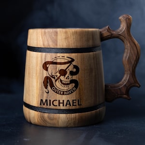 May include: A wooden beer stein with a black band around the top and bottom. The stein has a skull and snake design with the words "Outer Haven" and the name "Michael" engraved on it.