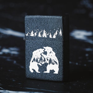 Puede incluir: Encendedor negro con un dise&ntilde;o blanco de dos osos enfrentados. Los osos est&aacute;n rodeados de una escena de bosque y estrellas.