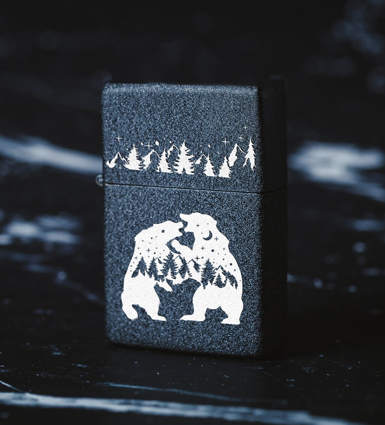 Puede incluir: Encendedor negro con un dise&ntilde;o blanco de dos osos enfrentados. Los osos est&aacute;n rodeados de una escena de bosque y estrellas.