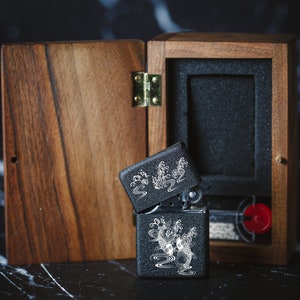 May include: A black lighter with a silver design of koi fish and waves in a wooden box. The box is open and the lighter is partially out of the box.