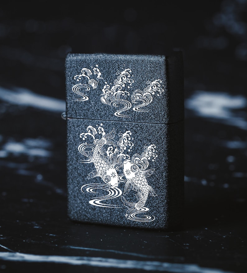 May include: A black lighter with a white design of two koi fish swimming in a wave pattern.