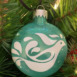 May include: Teal blue Christmas ornament with a white glitter finish and a white dove design.