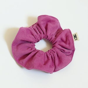 Op de afbeelding: Een roze scrunchie van corduroy met een klein label met de tekst "M LILA".