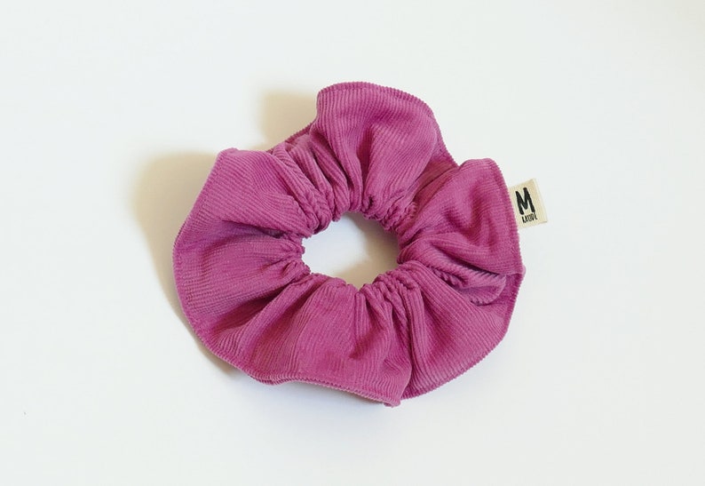 Op de afbeelding: Een roze scrunchie van corduroy met een klein label met de tekst "M LILA".