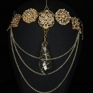 May include: Gold chain headpiece with a large clear crystal pendant. The headpiece features multiple chains and ornate gold metalwork with clear rhinestones.