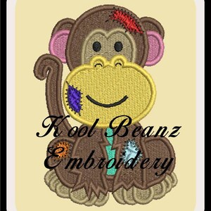Op de afbeelding: Borduurwerk van een bruine aap die een gele cirkel met een glimlachend gezicht vasthoudt. De aap heeft roze oren en een rood en bruin plekje op zijn hoofd. Het ontwerp bevat de tekst "Kool Beanz Embroidery".
