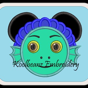 Op de afbeelding: Borduurwerk van een groene vis met blauwe en paarse details, die zwarte Mickey Mouse-oren draagt. De vis heeft gele ogen en een kleine mond. De tekst "Koolbeanz Embroidery" is zichtbaar onder de vis.
