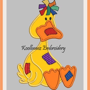 Könnte beinhalten: Eine gelbe Patchwork-Ente mit einer bunten Schleife auf dem Kopf. Die Ente sitzt mit den Füßen zusammen. Der Text "Koolbeanz Embroidery" befindet sich unter der Ente.