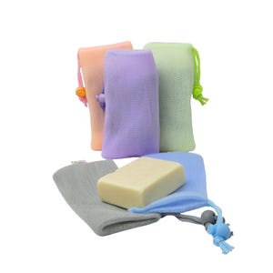 May include: A collection of colorful soap saver bags in shades of peach, lavender, and green, with a gray, blue, and gray bag holding a bar of soap. Each bag has a drawstring closure with a decorative bead.